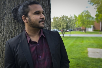 close up of Yash leaning on tree and looking off in the distance