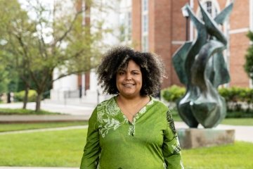 Lady with dark curly hair wearing green top standing in front of flame statue