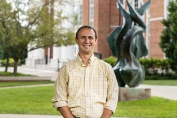 Man wearing yellow plaid button up dress shirt standing in front of the flame statue