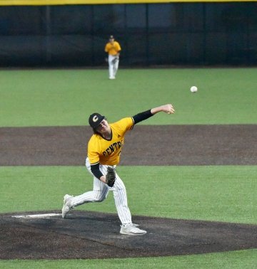 A baseball player releases a ball from the pitching mound as an outfielder watches in the background. 