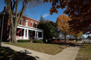 A two-story brick building with white columns is fronted by a small lawn and a sidewalk 