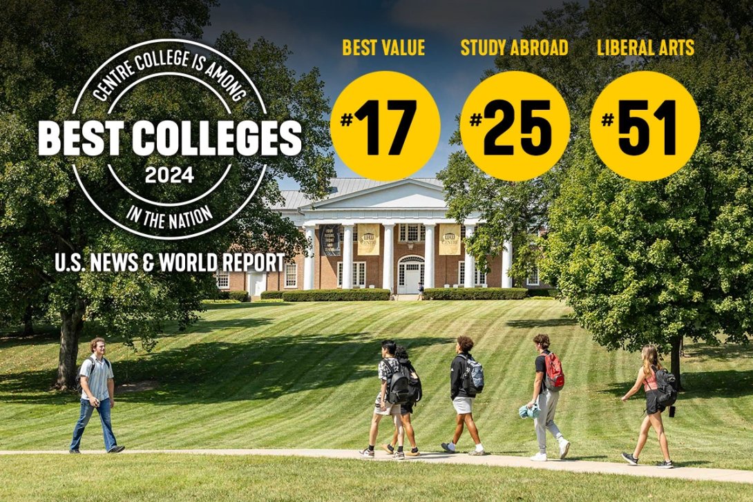 Students walk along a sidewalk in with a long green lawn leading to a brick building with columns in the background.