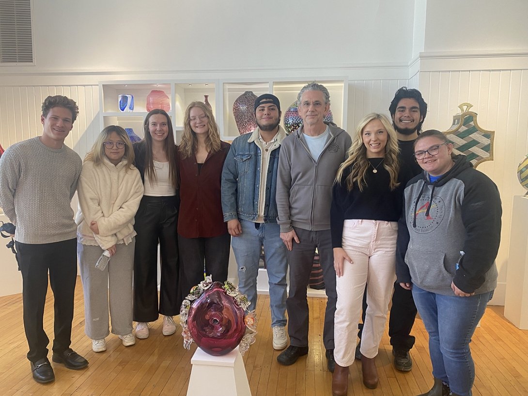 Students pose for a photo behind their contributed piece to the GLASS National Art Museum.