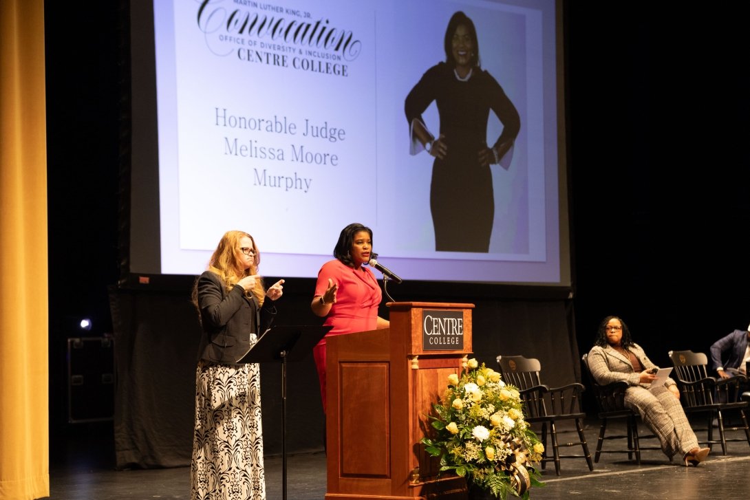 MLK convo 2024. Two ladies standing by podium. One lady sitting on stage in Newlin Hall. Photo by Lucy Swenson '24