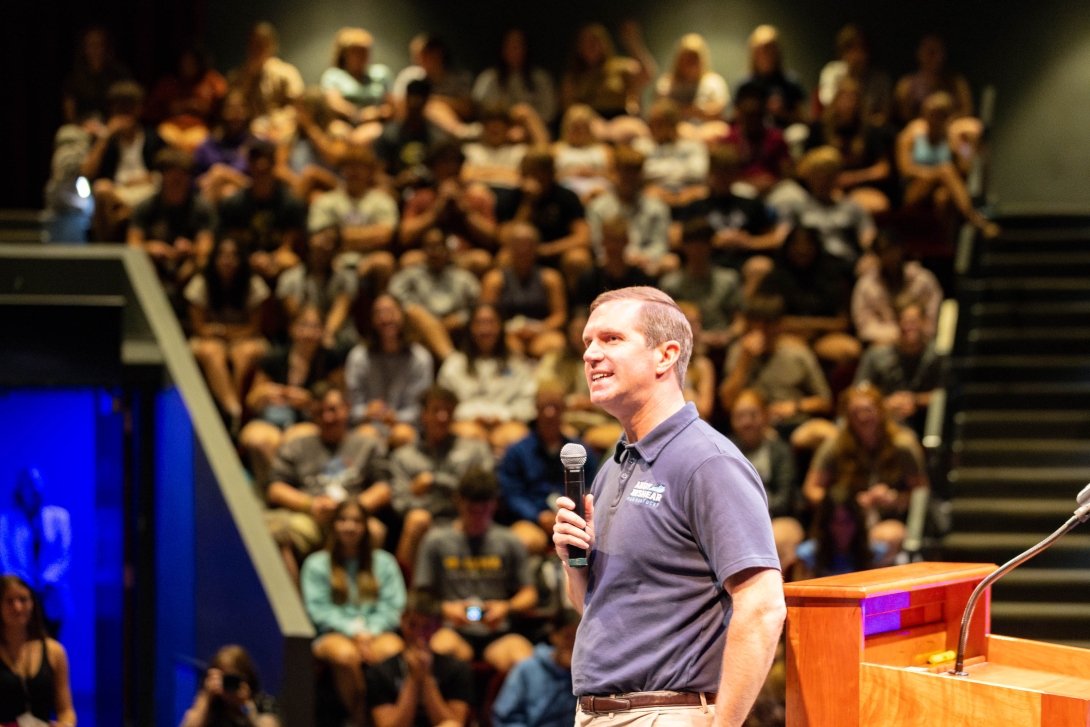 A man with a microphone talks to an audience.