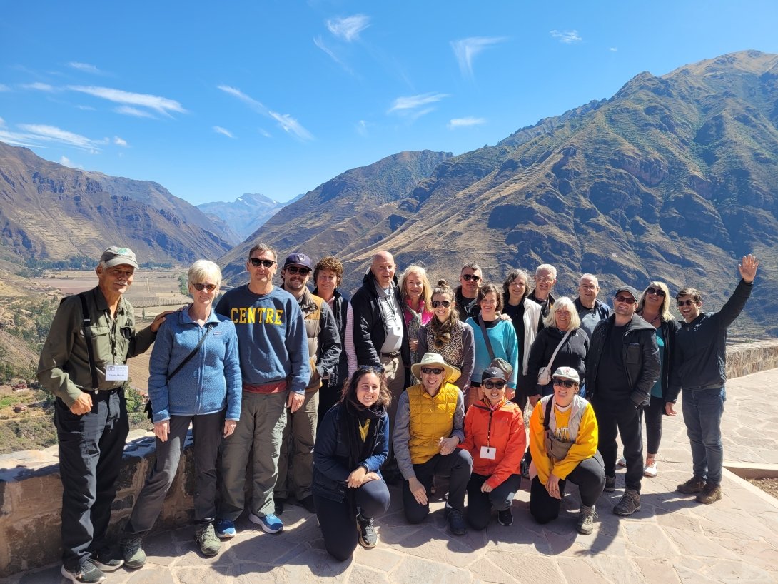A large group poses for a photo on an overlook with rugged mountains and a valley behind them. 