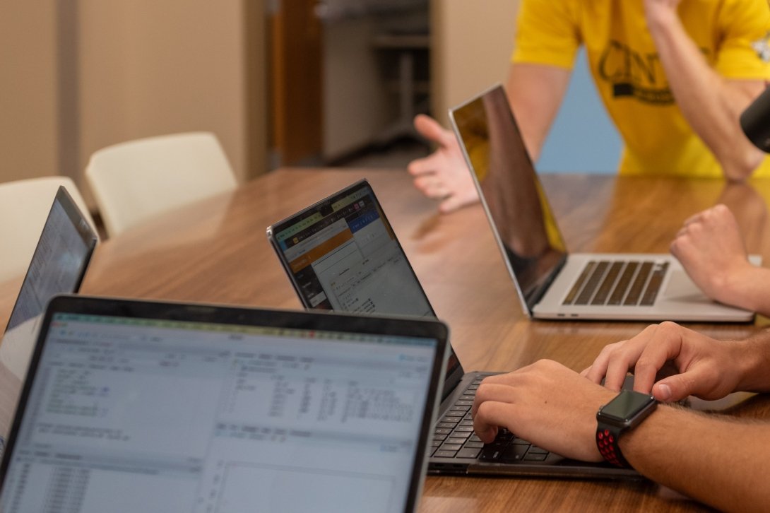 Open laptop computers are seen on a table with hands working on the keyboards.