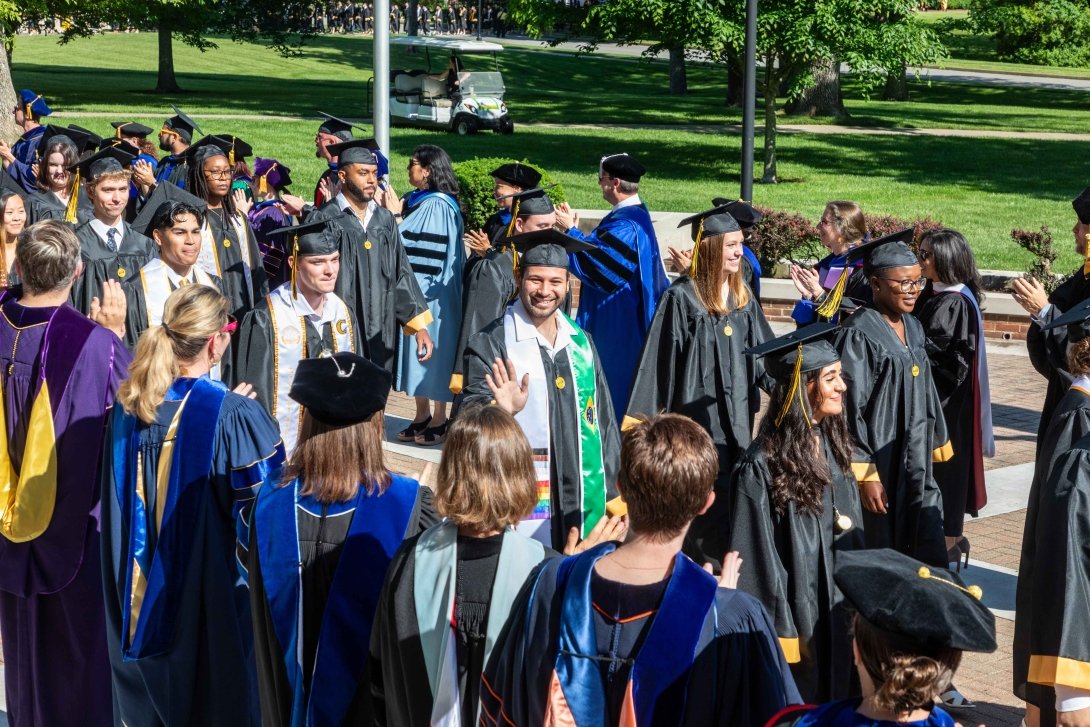Honor walk ceremony where students in regalia walk past all their faculty members who are clapping for them at commencement.