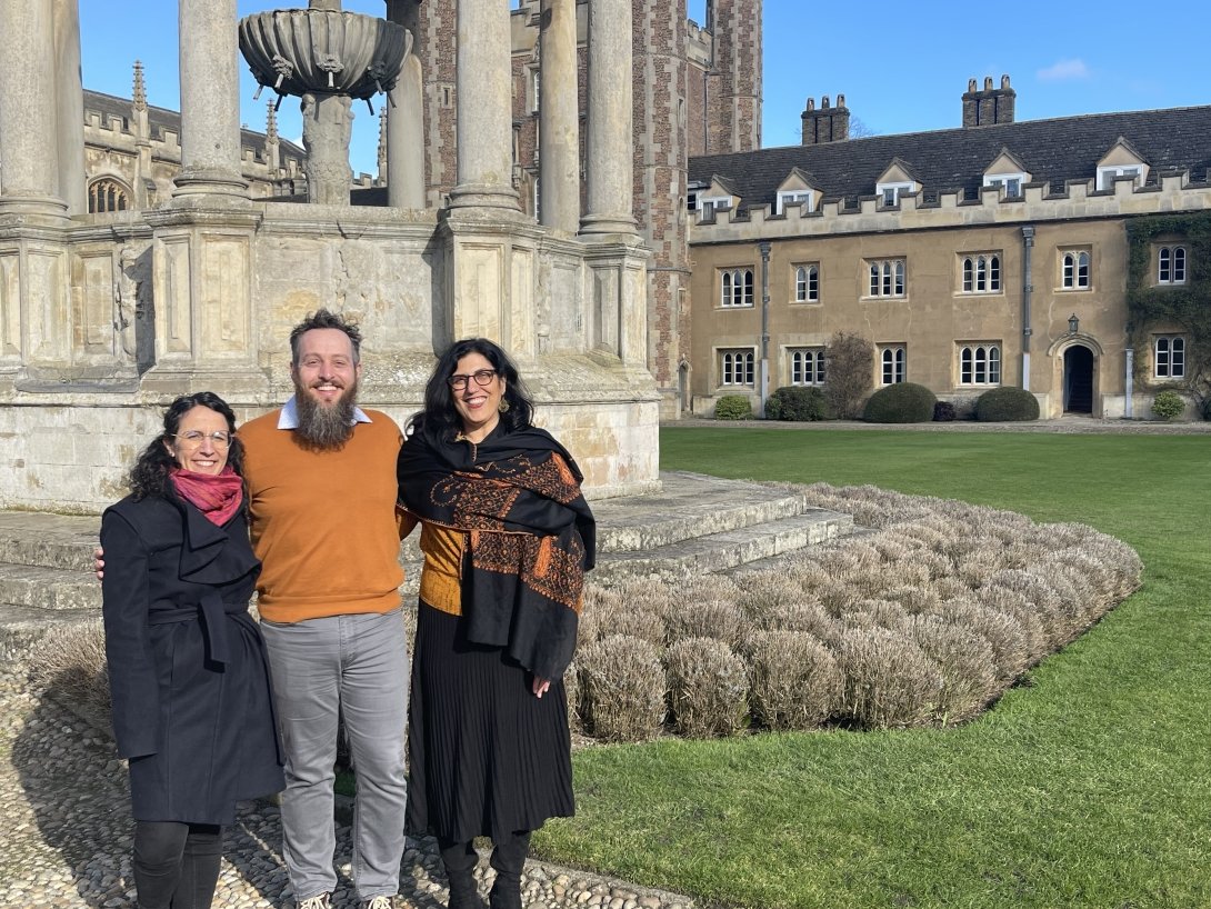 A man stands between two women, posing for a photo in front of historic stone buildings.