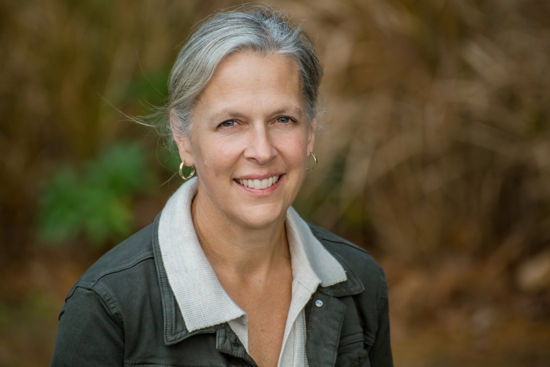 A woman wearing a collared shirt and a jacket poses for a photo outdoors. 