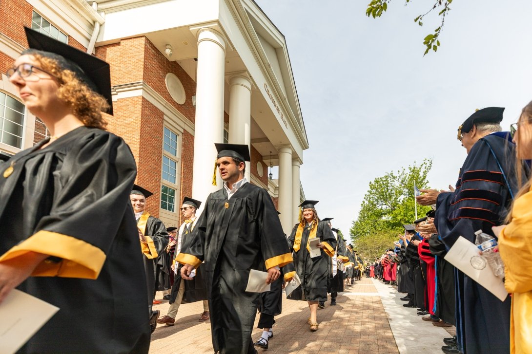 Graduates walking in front of Crounse Hall while being applauded by faculty and staff.