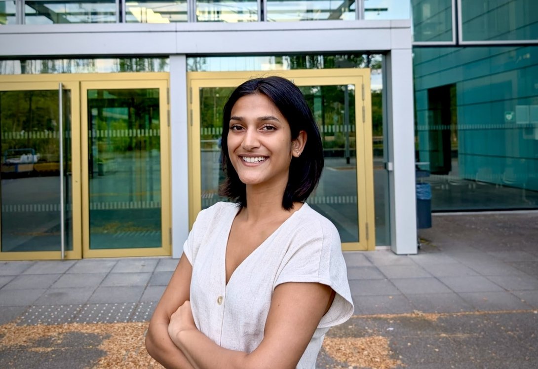 Mehak Mittal is smiling and standing in front of doors to a building, posing for a headshot.