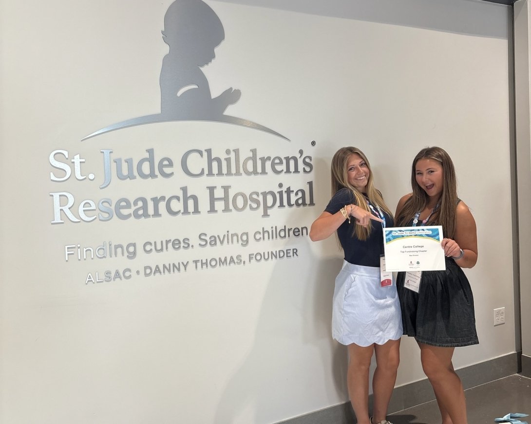 Two Tri-Delta leaders are standing in front of a St. Jude sign holding their philanthropy award.