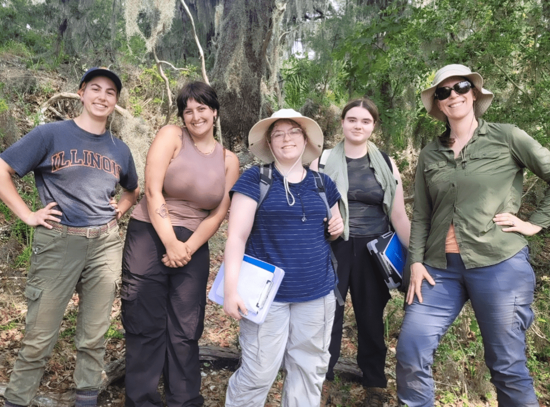 A group of students and faculty are smiling while wearing gear for an Archaeological dig.