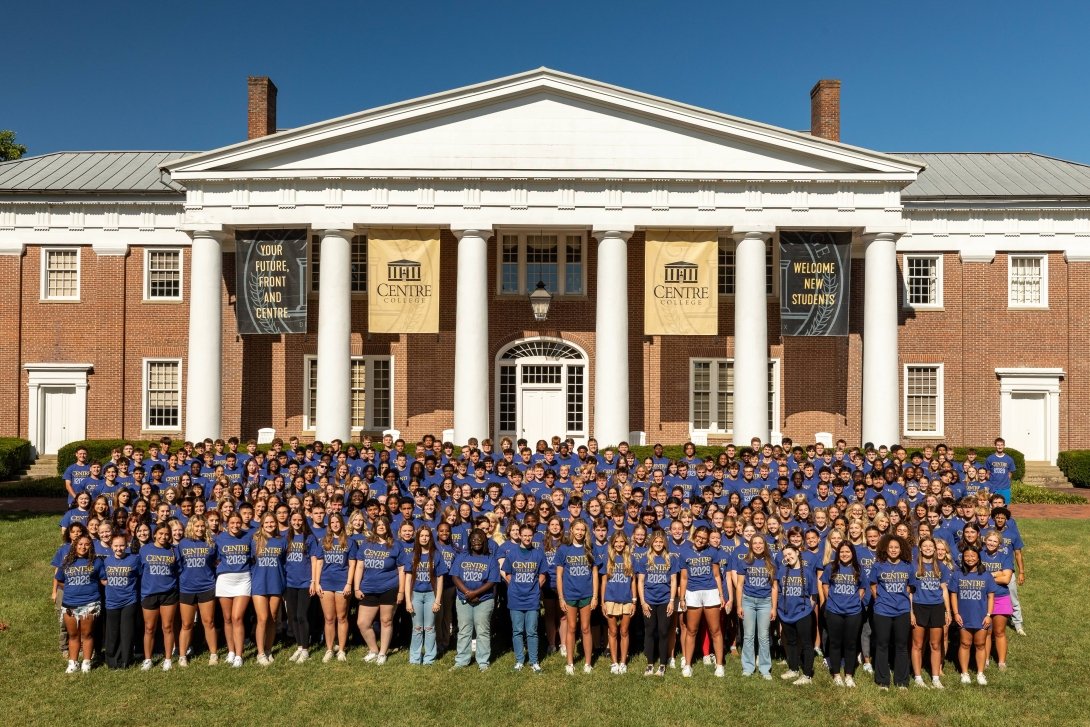 A group photo of the class of 2029. They are all standing in front of Old Centre and wearing bright blue shirts.