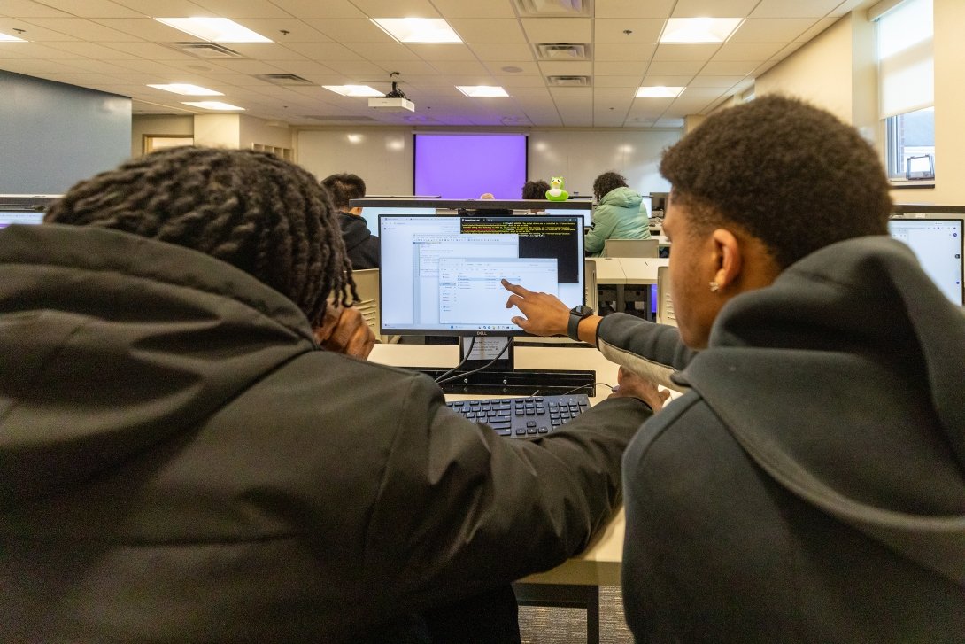 Two Centre College students huddle around a computer screen as one points to a portion of code during Professor Thomas Allen's AI class. 
