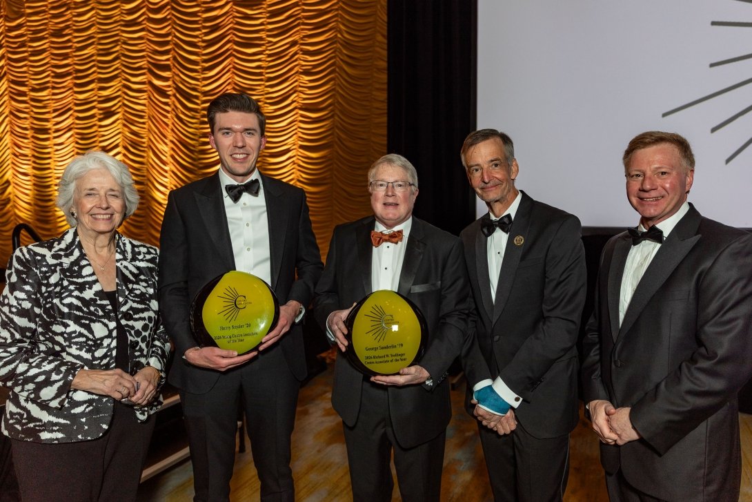 One woman stands alongside four men in tuxedos, two holding gold and black Associate of the Year awards.