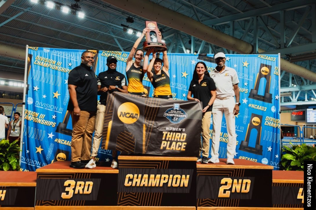 Hein and McNeilly stand on the podium holding the team award, surrounded by their coaches.