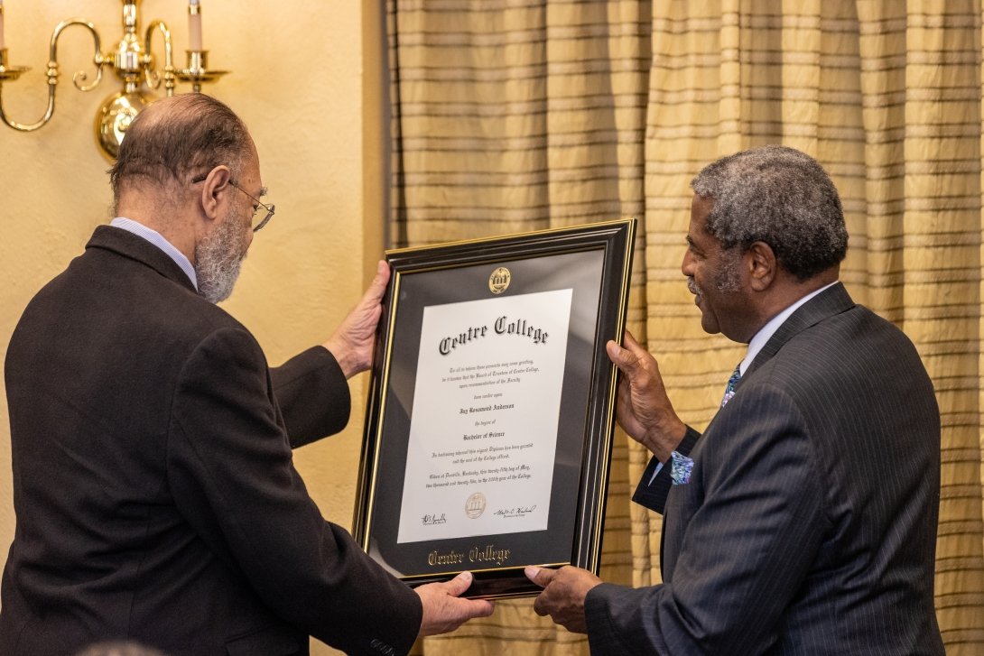 Two men, Dr. Jay Anderson and Raymond Burse, hold a framed Centre College degree while reading the text together. 