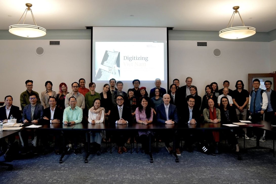 Two rows of people pose for a photo in front of a projector screen during a Digitizing Vietnam conference at Columbia University. 