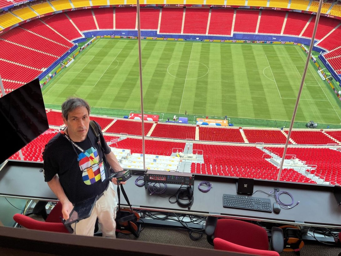 Dave Schoonaert is behind a tech table, with a view of the Kansas City FIFA World Cup Stadium.